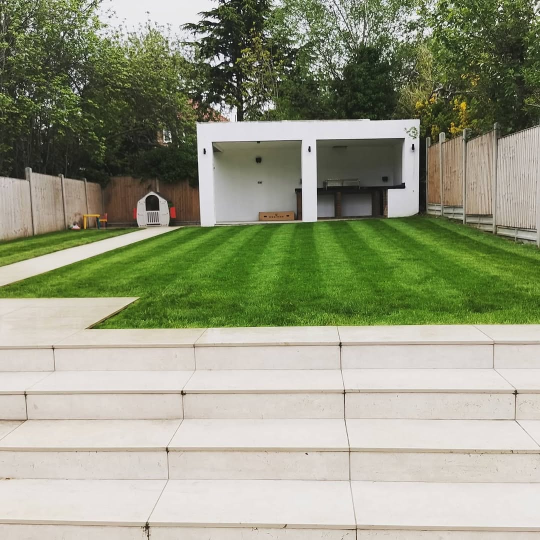A stepped garden leading down to a modern white pool house, with a striped lawn