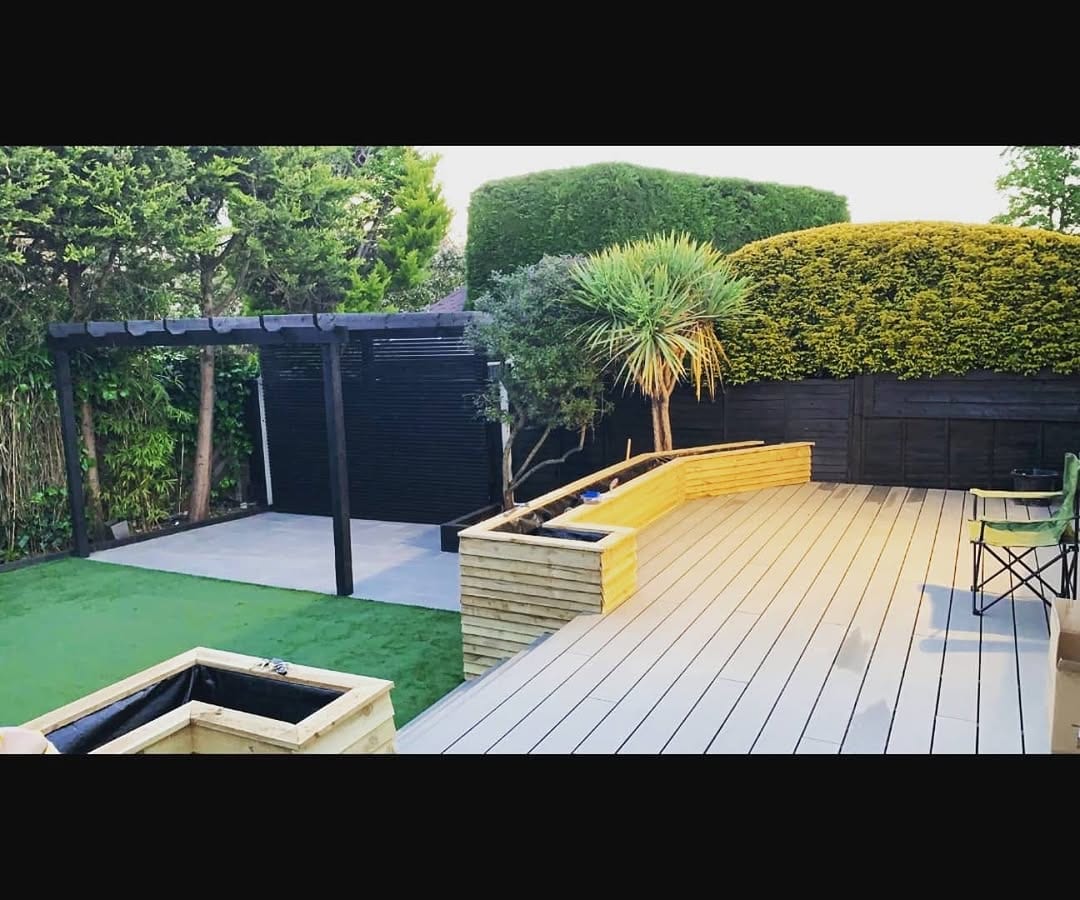 A modern garden with a black pergola, composite decking, artificial lawn, and raised planters