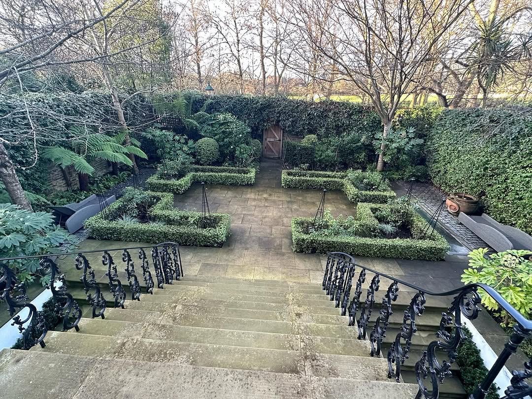 A formal garden with clipped box hedges and tree ferns, reached by stone steps leading to a wooden door in a hedge